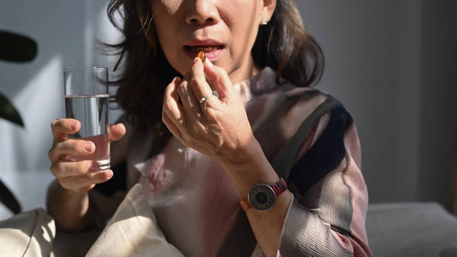Mature woman holding glass of fresh water, taking dietary supple