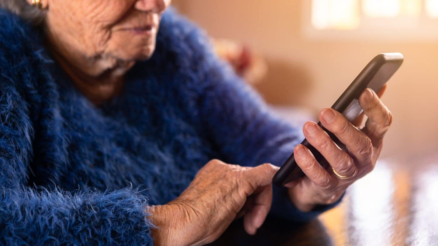 Elderly woman using mobile phone while sitting at living room home. Grandmother