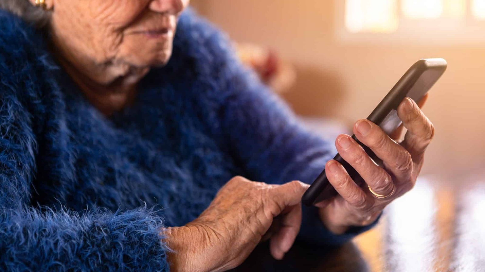 Elderly woman using mobile phone while sitting at living room home. Grandmother